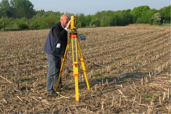 Mann steht mit Vermessungsgerät auf einem Feld