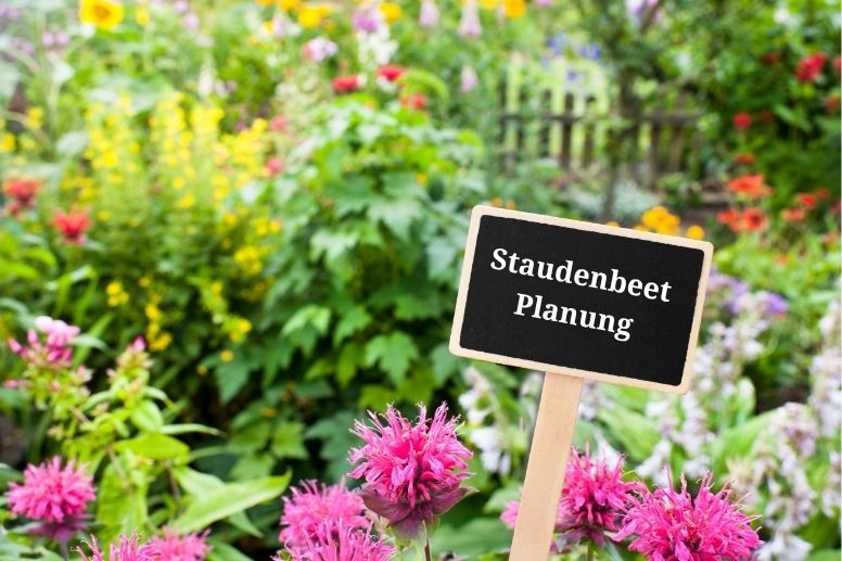 Staudenbeet mit blühenden Pflanzen, mit einer kleinen Holztafel. 